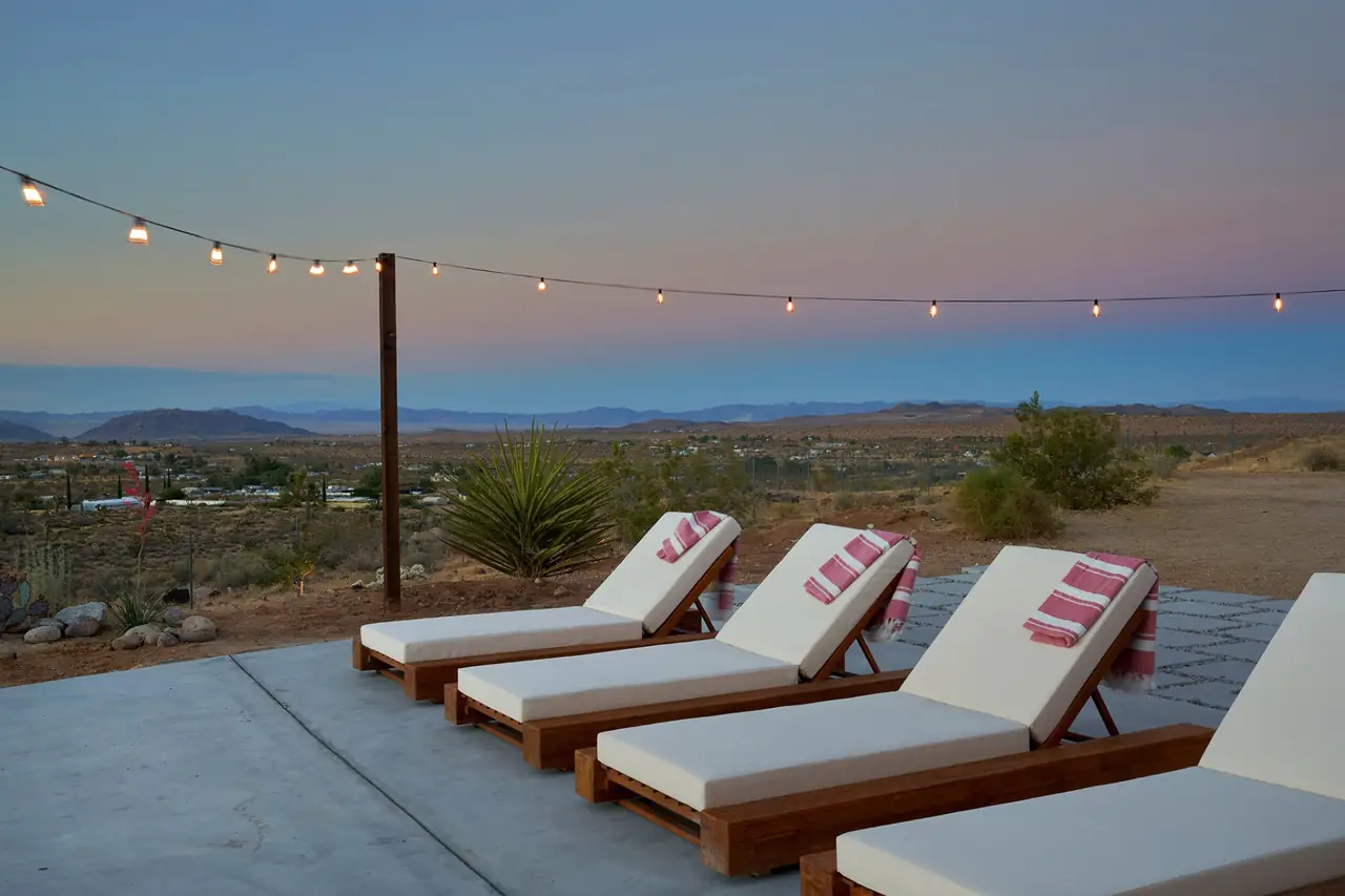Poolside chaise loungers at dusk with string lights