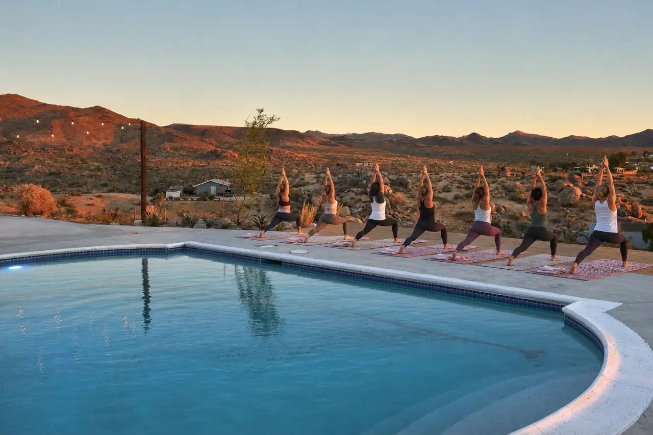 Yoga class in warrior pose beside pool at sunrise